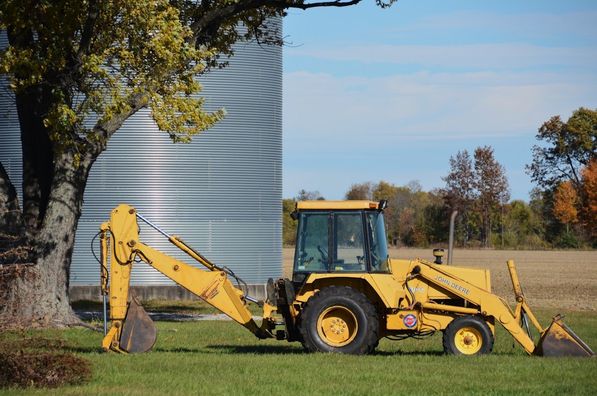 Backhoe loader parked beside a grain silo in bright daylight